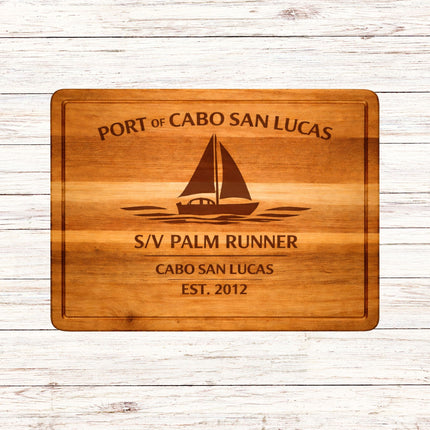 Wooden cutting board with engraved text and sailboat design on a wooden surface