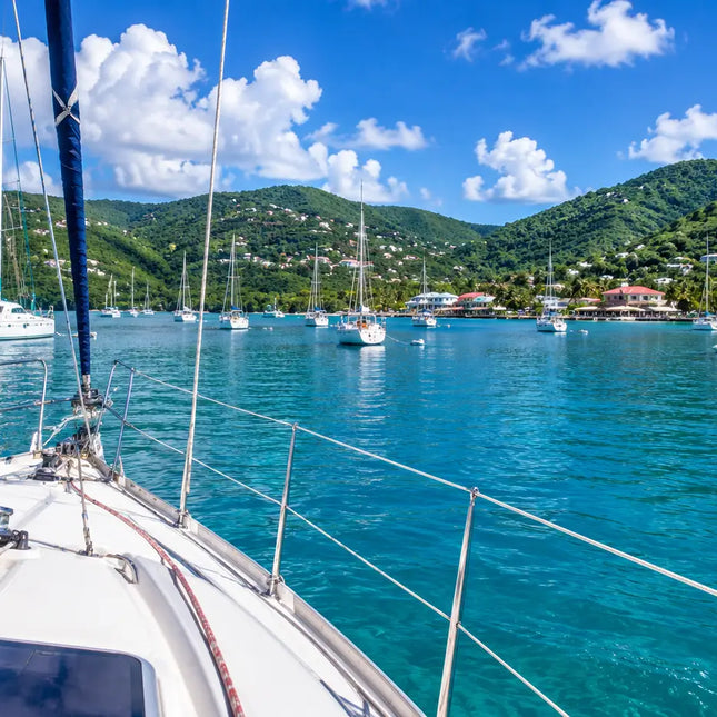 View from the cockpit of a cruising sailboat arriving in Coral Bay, St. John, U.S. Virgin Islands, with anchored sailboats, calm turquoise waters, and the peaceful waterfront ahead.