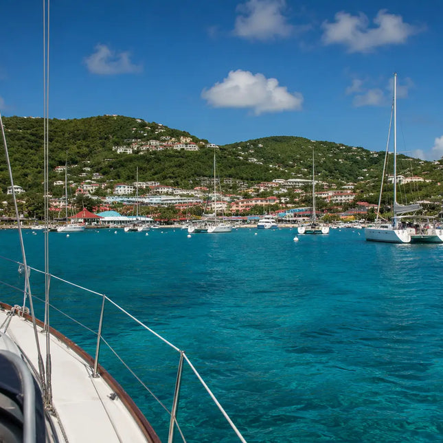 View from the deck of a sailboat arriving in Cruz Bay Harbor, St. John, U.S. Virgin Islands, with anchored yachts, white mooring balls, and the colorful waterfront ahead.