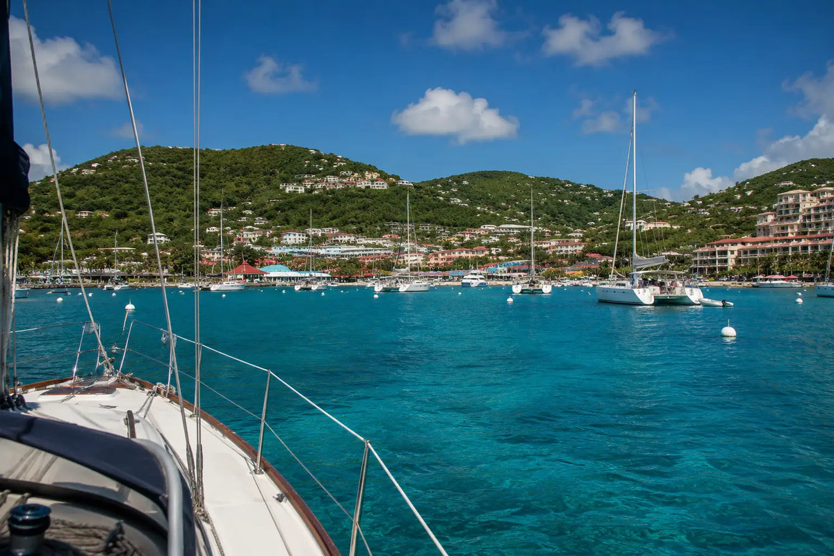 View from the deck of a sailboat arriving in Cruz Bay Harbor, St. John, U.S. Virgin Islands, with anchored yachts, white mooring balls, and the colorful waterfront ahead.