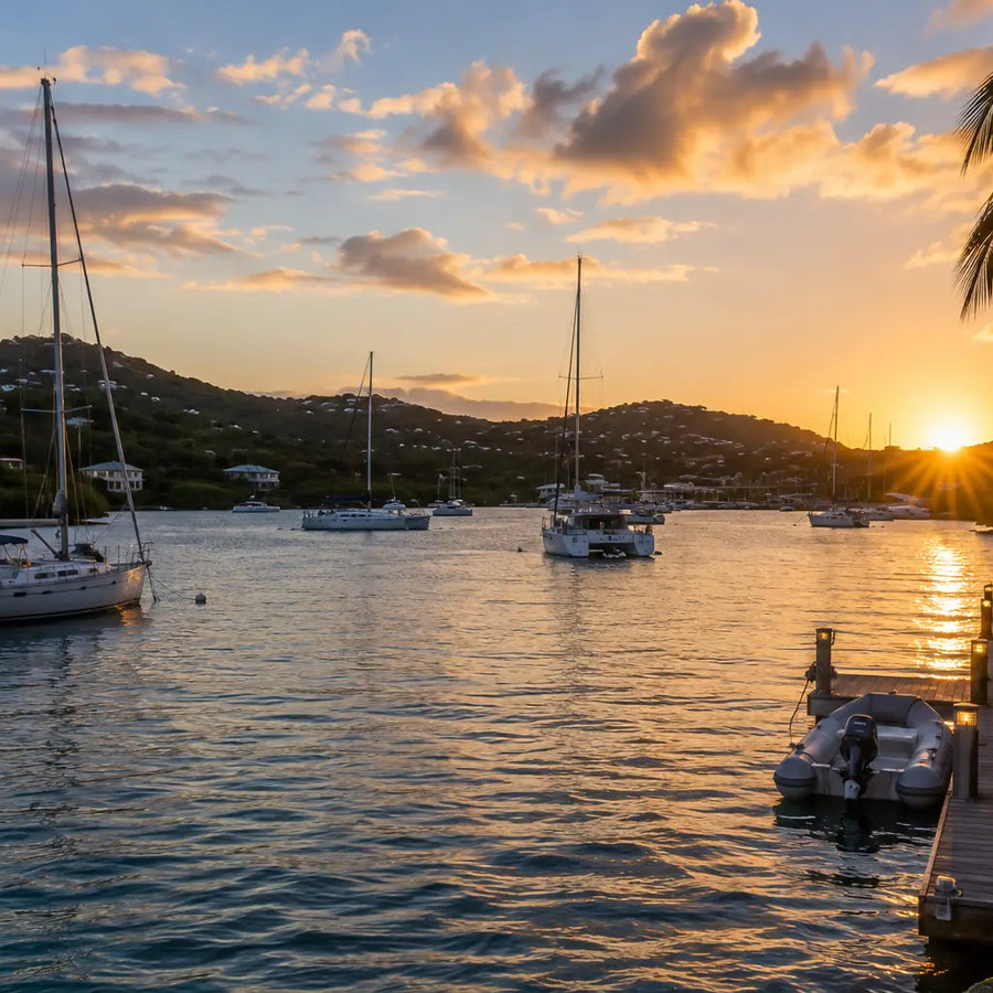 Sunset over Benner Bay Harbor with anchored sailboats, waterfront docks, and a peaceful Caribbean cruising atmosphere.