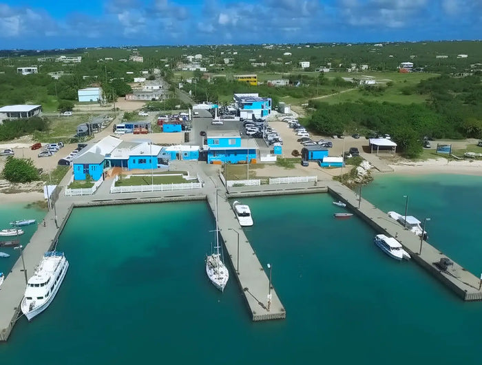 Aerial view of Blowing Point Harbor in Anguilla showing the ferry terminal, docks, sailboats, and turquoise Caribbean waters.