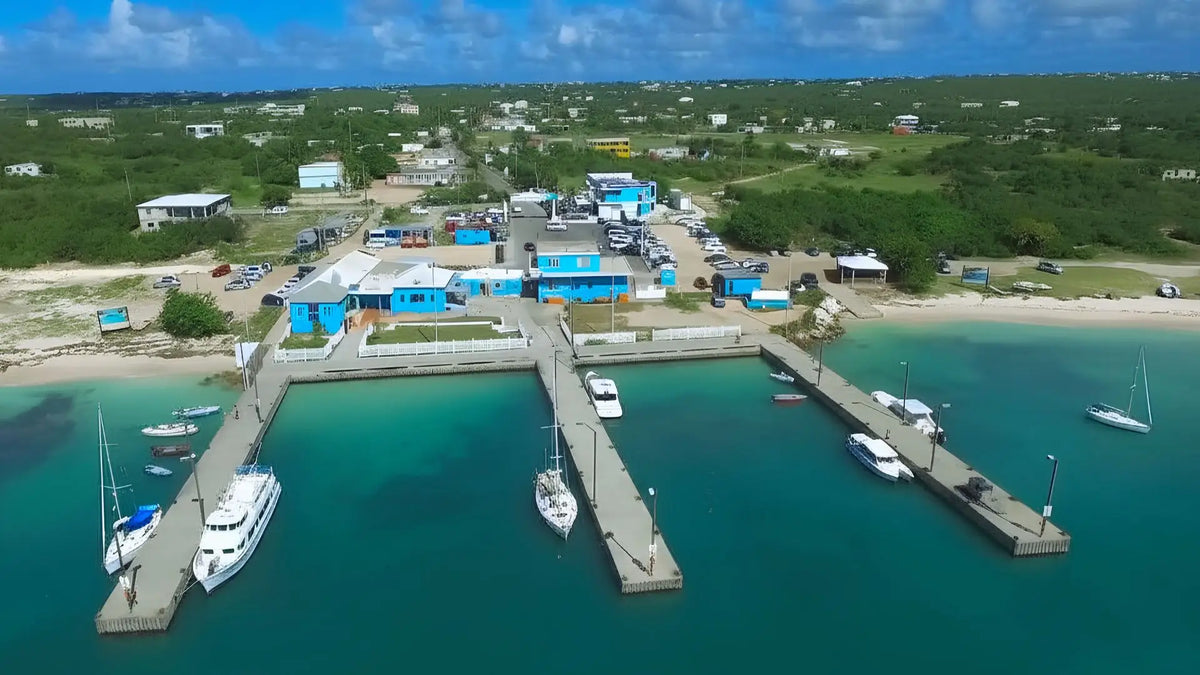 Aerial view of Blowing Point Harbor in Anguilla showing the ferry terminal, docks, sailboats, and turquoise Caribbean waters.