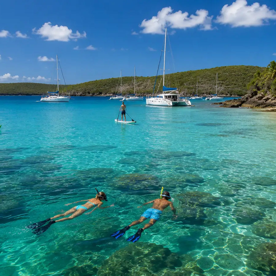Snorkelers exploring the clear waters of Christmas Cove with anchored catamarans and tropical shoreline in the background.