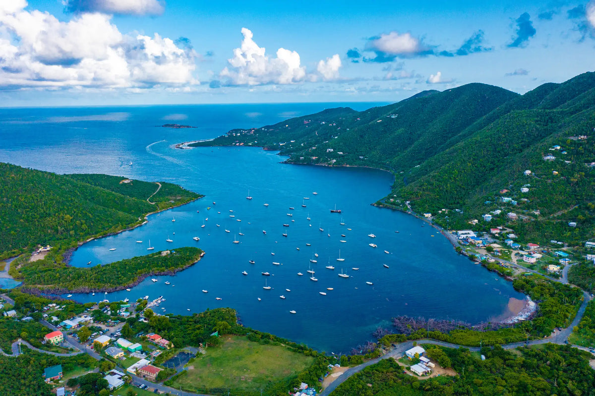 Aerial view of Coral Bay Harbor in St. John, U.S. Virgin Islands, showing the protected harbor, sailboats on moorings, lush tropical hills, and the quiet waterfront village.