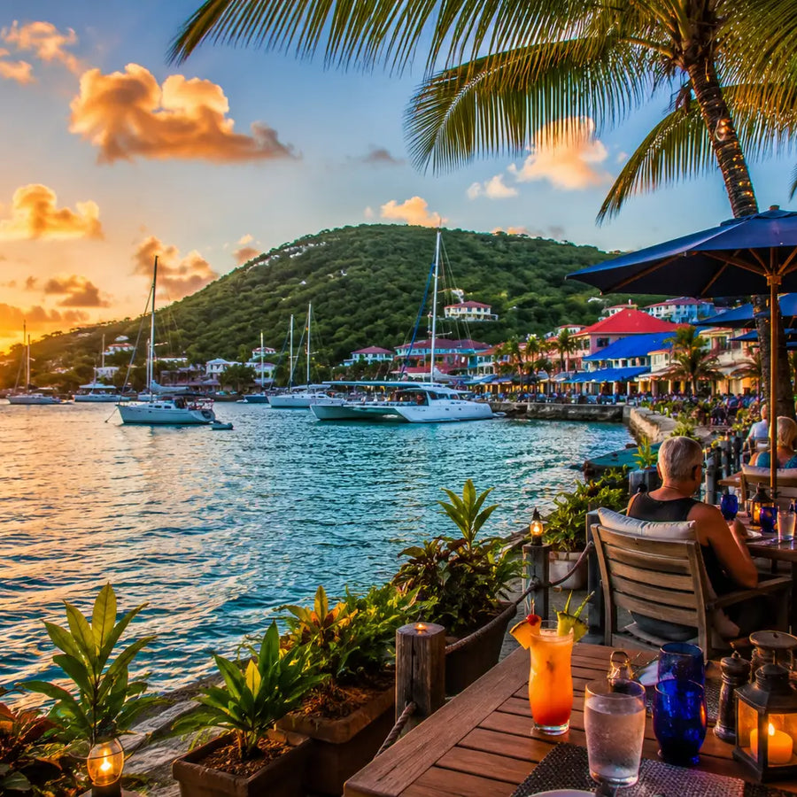 Outdoor waterfront dining overlooking Cruz Bay Harbor in St. John, U.S. Virgin Islands, with sailboats, palm trees, colorful buildings, and a Caribbean sunset.