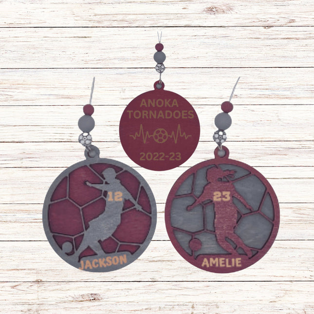 Soccer-themed earrings with 'Anoka Tornados' and player names on a wooden background