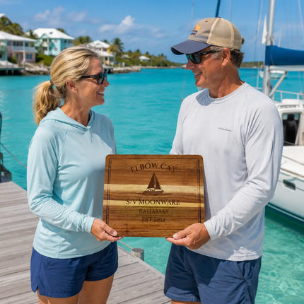 Elbow Cay Bahamas personalized cutting board being exchanged as a gift beside calm harbor water and cruising sailboats in the Abacos