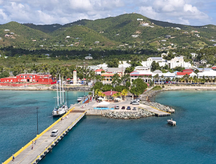 Aerial view of Frederiksted Harbor and waterfront on St. Croix, U.S. Virgin Islands, featuring the cruise pier, turquoise Caribbean waters, historic town, and lush green hills.