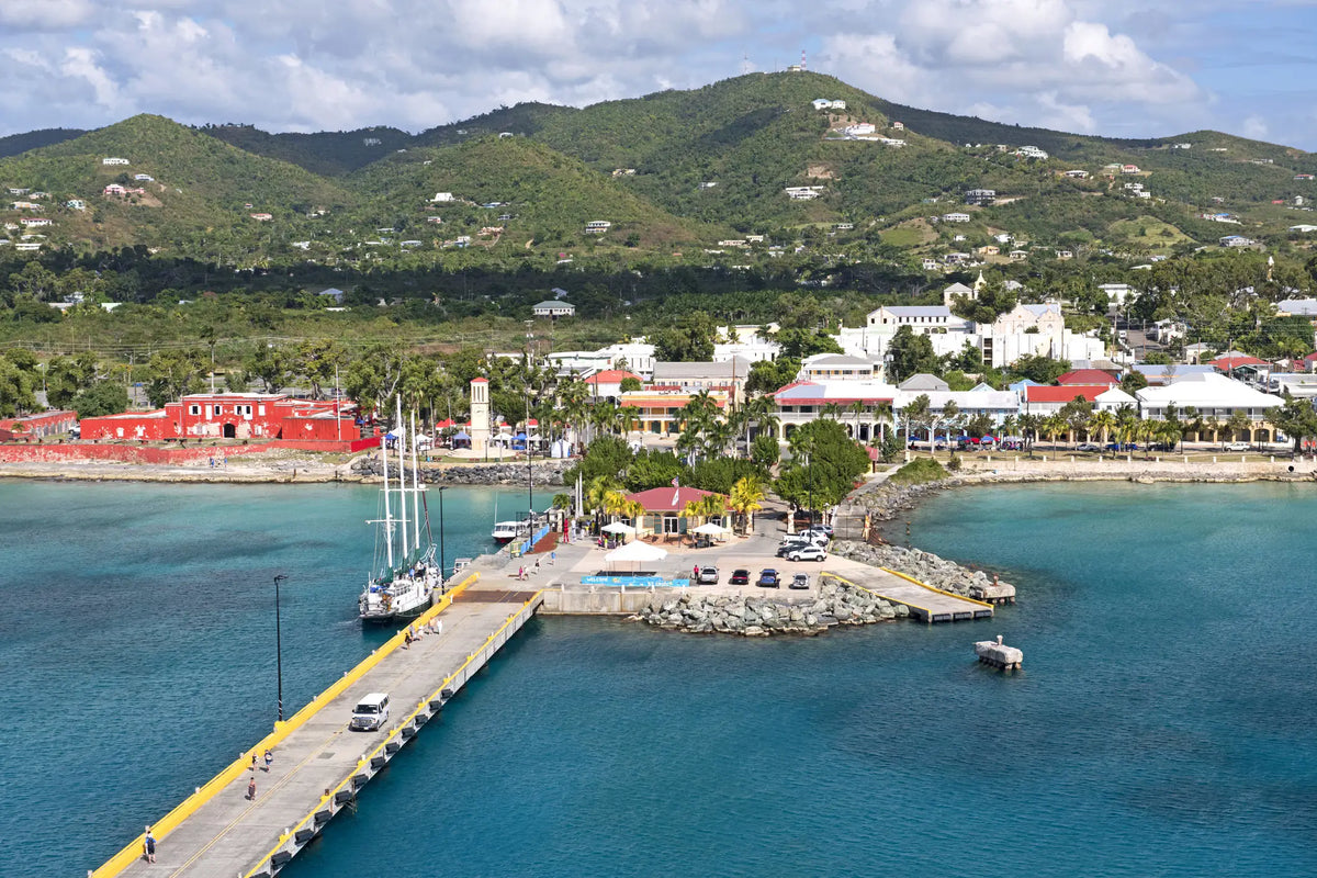Aerial view of Frederiksted Harbor and waterfront on St. Croix, U.S. Virgin Islands, featuring the cruise pier, turquoise Caribbean waters, historic town, and lush green hills.