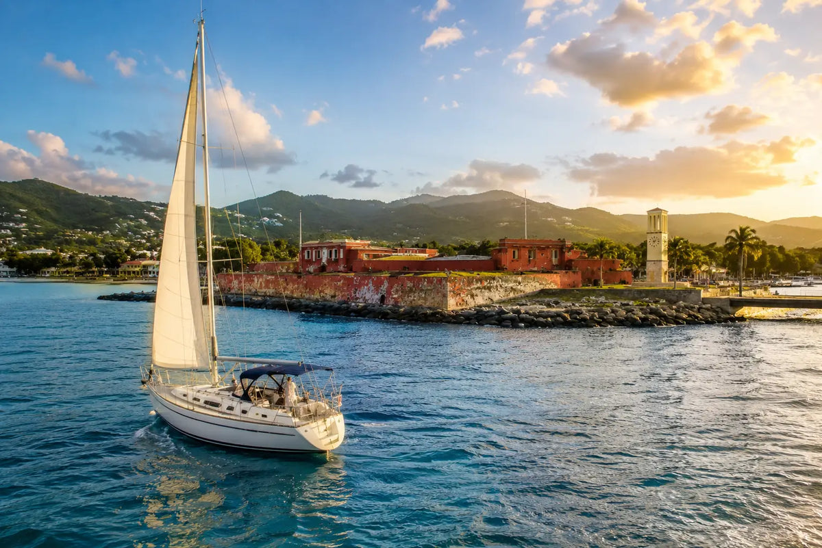 Sailboat departing Frederiksted Harbor along the west coast of St. Croix, U.S. Virgin Islands, with Fort Frederik, turquoise Caribbean waters, and lush green hills in the background.