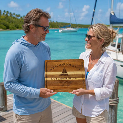 Great Harbour Cay Bahamas personalized cutting board being exchanged as a gift beside calm turquoise harbor water and anchored cruising sailboats