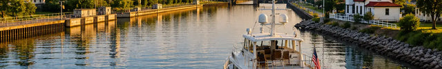 Luxury trawler yacht cruising through a calm Great Loop waterway at sunset with lighthouse, marina channel, and city skyline in the background.