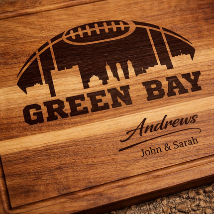 Close-up of dark laser engraved Green Bay football skyline and personalized family name carved into solid acacia wood cutting board
