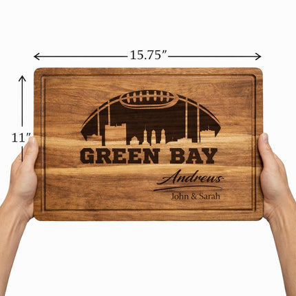 Personalized Green Bay football cutting board held in hands showing full size and thickness, measuring 15.75 by 11 inches with dark laser engraving on solid acacia wood
