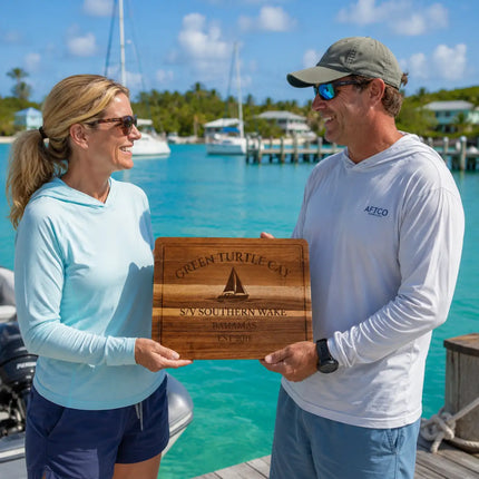 Green Turtle Cay Bahamas personalized cutting board being exchanged as a gift near a quiet dock with anchored sailboats and calm turquoise water