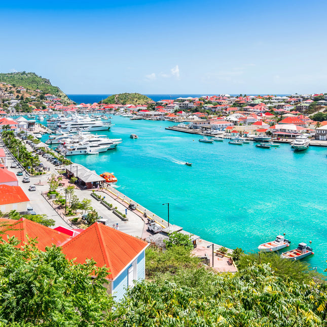 Luxury yachts and turquoise waters in Gustavia Harbor, St. Barths, featuring the waterfront marina and red-roofed Caribbean buildings.