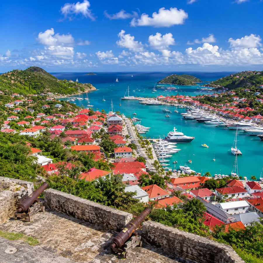Panoramic view overlooking Gustavia Harbor in St. Barthélemy featuring red-roofed buildings, turquoise waters, anchored yachts, and surrounding Caribbean hills