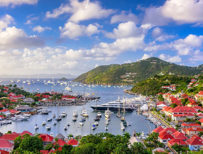 Panoramic view of Gustavia Harbor in St. Barths with sailboats, luxury yachts, red-roofed buildings, and Caribbean waters.