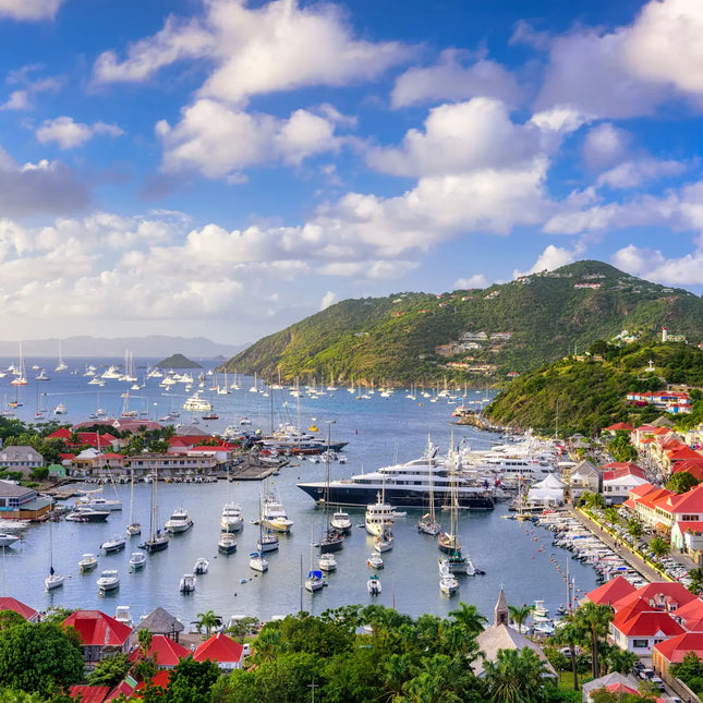 Panoramic view of Gustavia Harbor in St. Barths with sailboats, luxury yachts, red-roofed buildings, and Caribbean waters.