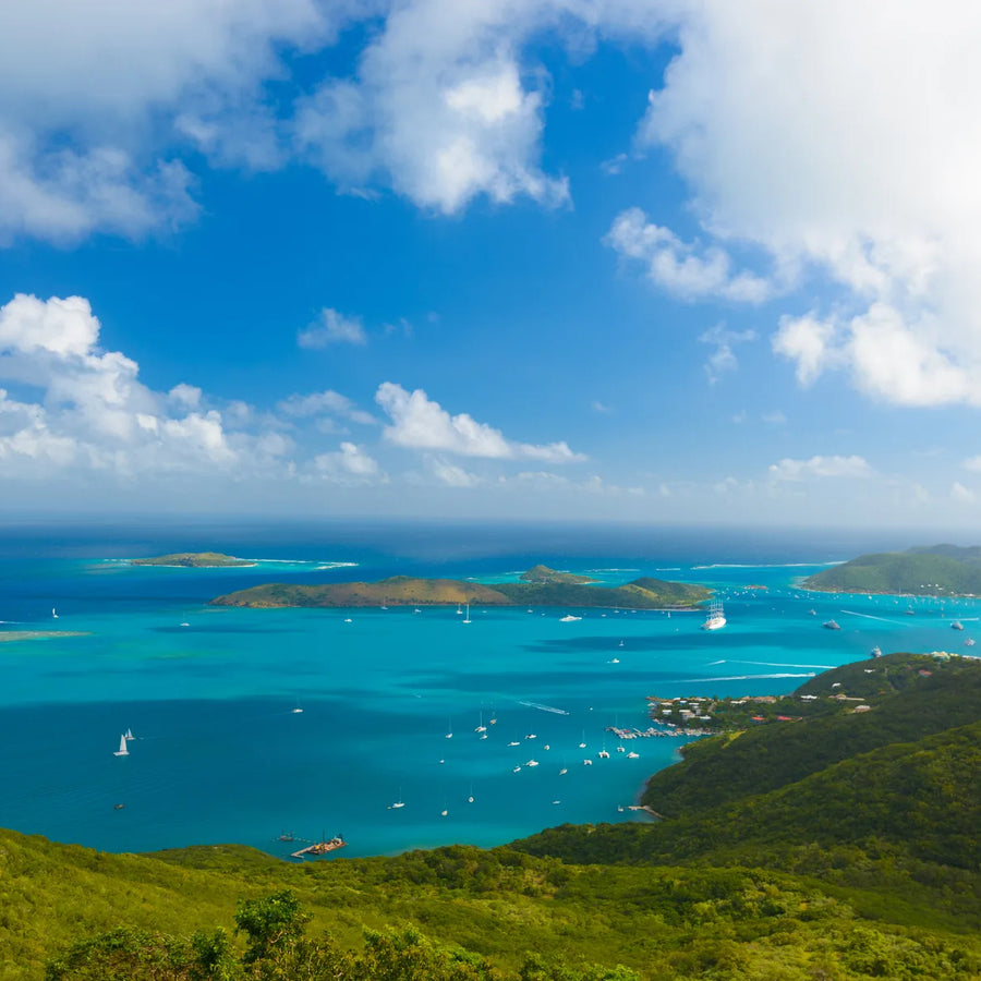 Elevated view across North Sound, with turquoise water, scattered sailboats, green islands, and clouds overhead.