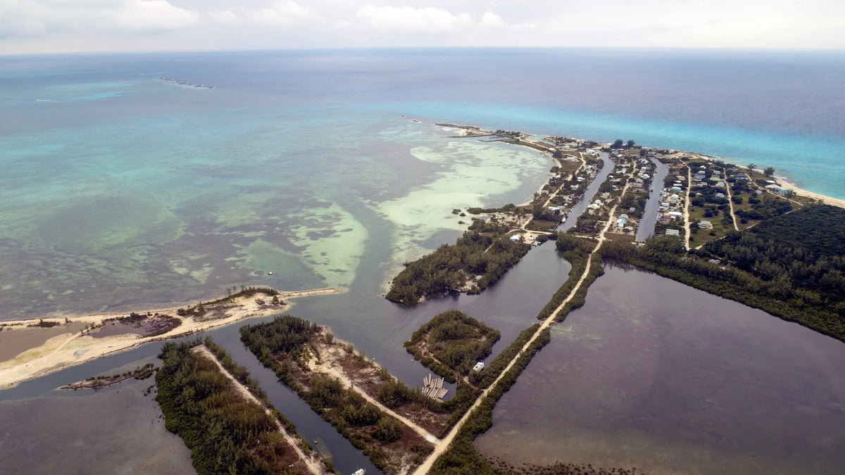 Waterfront homes and narrow waterways border low vegetation, pale sand and broad areas of blue-green coastal water.