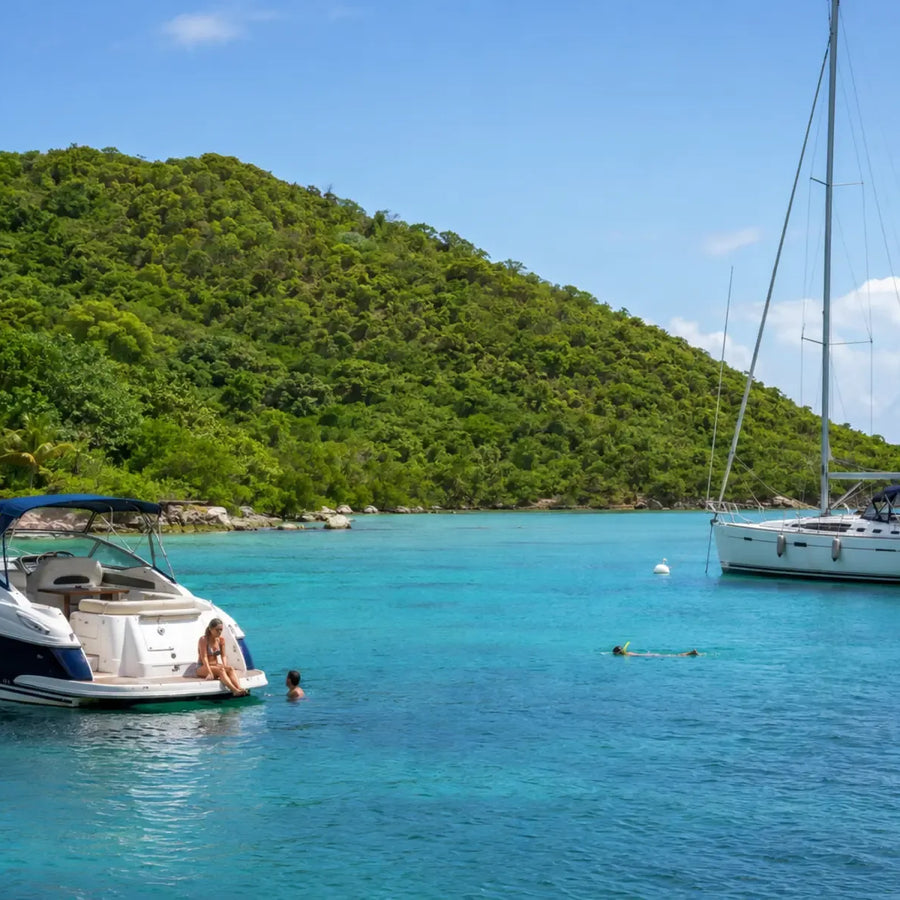 A power cruiser and sailboat anchored near Virgin Gorda as people swim in calm turquoise water below lush green hills.