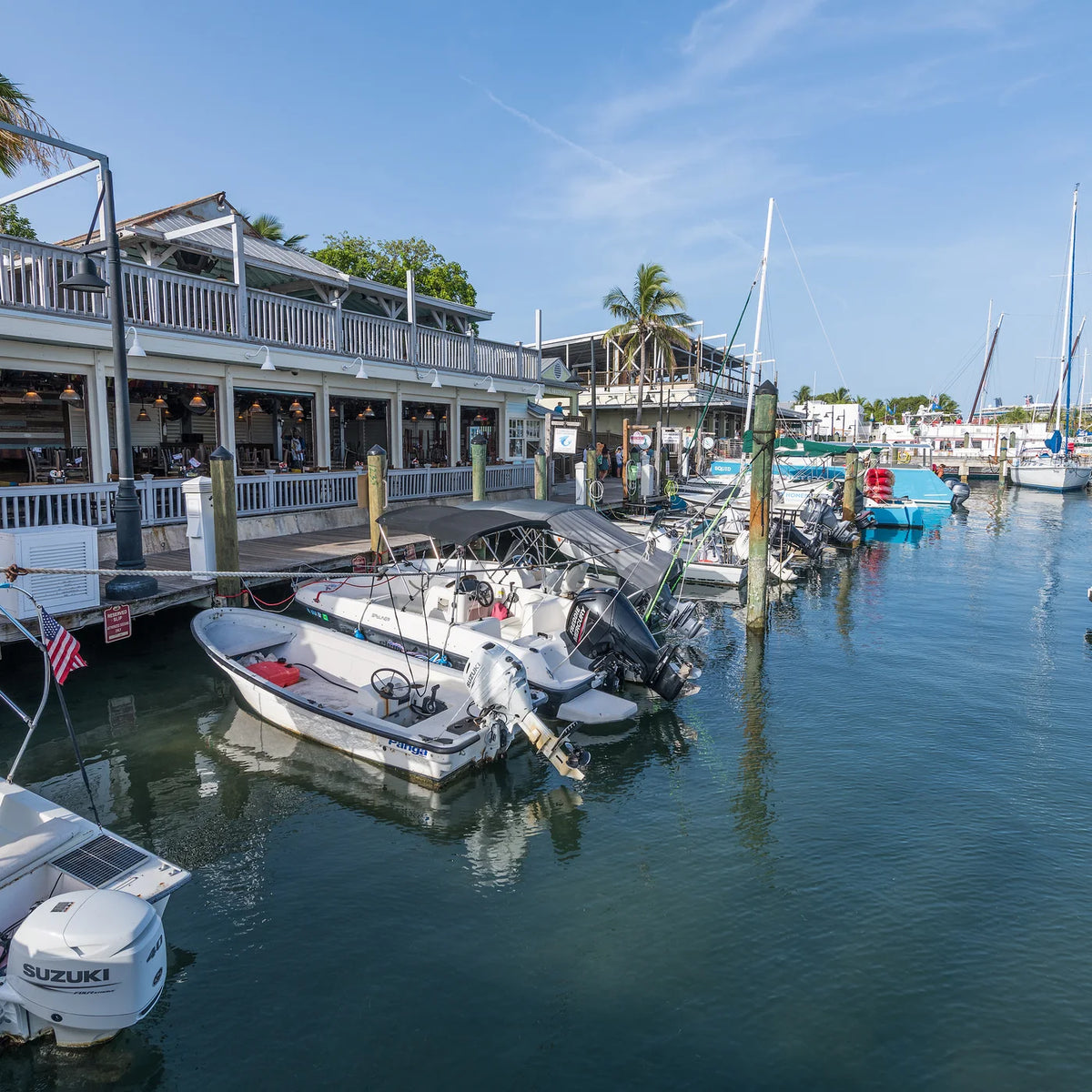 Dockside view of small motorboats, sailboat masts and a two-story waterfront building in Key West.