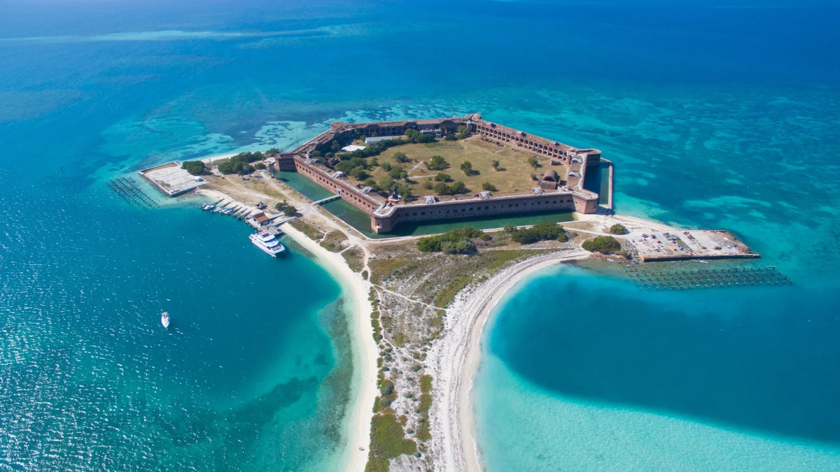 Aerial view of Fort Jefferson and its moat, curving white beaches, docked boats, and surrounding turquoise and deep-blue water.