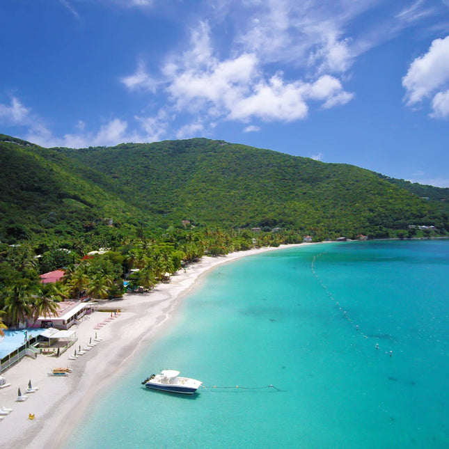 Elevated view along Cane Garden Bay’s curved beach, with a sailboat in turquoise water and green Tortola hills beyond.