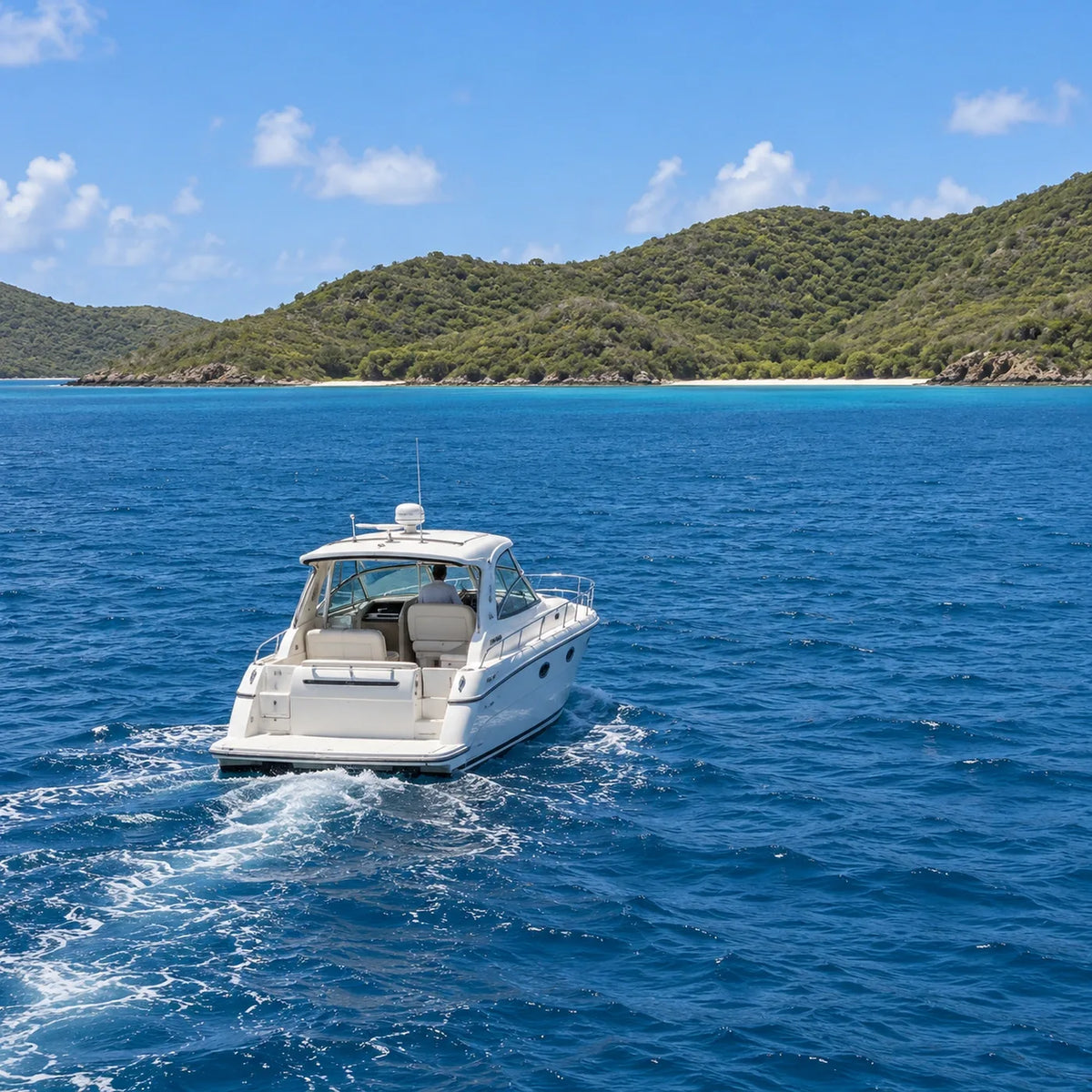 Stern view of a white cabin cruiser leaving a gentle wake across blue water toward low wooded hills and a narrow beach.