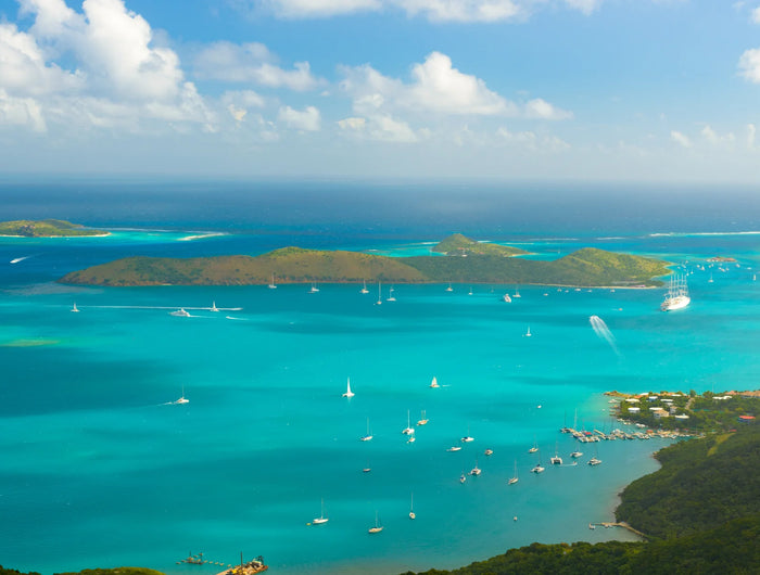 Aerial view of numerous sailboats and cruising vessels across turquoise water among green islands near Virgin Gorda.