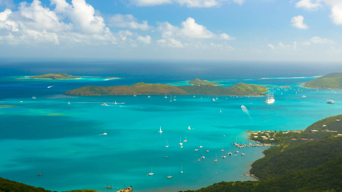 Aerial view of numerous sailboats and cruising vessels across turquoise water among green islands near Virgin Gorda.