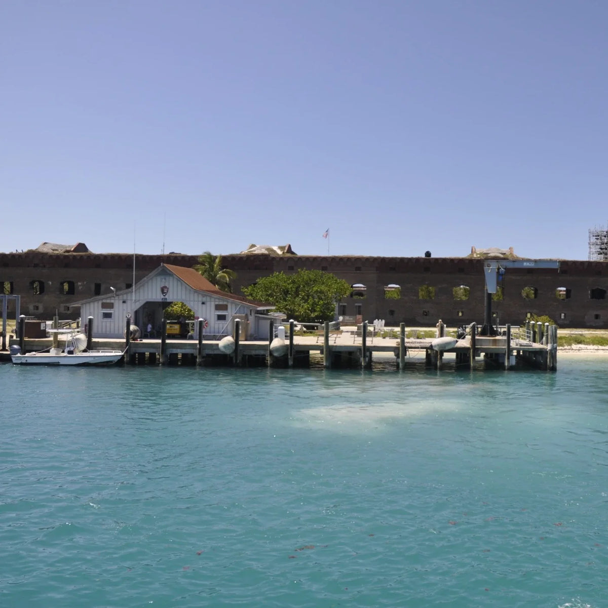 White dock house and small boat beside Garden Key’s pier, with Fort Jefferson’s brick walls behind.