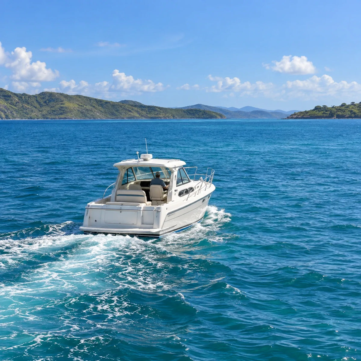 A white power cruiser travels across blue water toward green coastal hills, leaving a wake behind.
