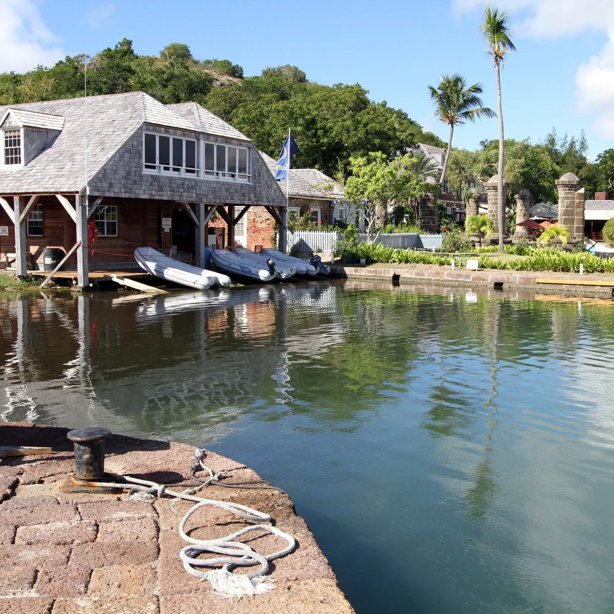 Inflatable dinghies beside a waterfront building, with palms, stone columns and a bollard and rope in the foreground.