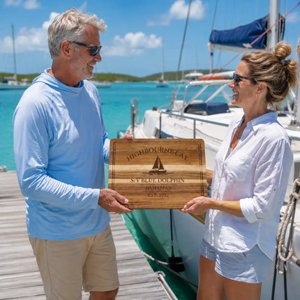Highbourne Cay Bahamas personalized cutting board being exchanged as a gift beside anchored catamarans and calm turquoise Exumas water
