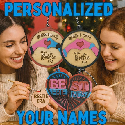 Two smiling young women sit at a holiday crafting table painting wooden best friend ornaments. Above them, colorful text reads “PERSONALIZED YOUR NAMES.” They hold round and heart-shaped wooden ornaments engraved with phrases like “Britta & Carly – In My Bestie Era” and “Best Friends.” The festive background includes a decorated Christmas tree and warm lighting, emphasizing the personalized DIY holiday theme.