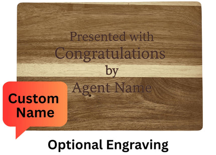 Image showing the back side of a personalized acacia wood cutting board with engraving that reads, “Presented with Congratulations by Agent Name.” A red speech bubble highlights “Custom Name.” Text above and below explains: “Reverse Side Sample – Woodgrains will vary” and “Optional Engraving for Realtor or Special Request.”