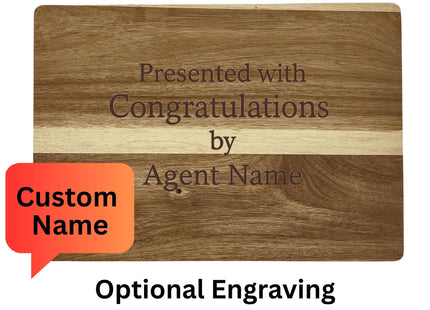 Image showing the back side of a personalized acacia wood cutting board with engraving that reads, “Presented with Congratulations by Agent Name.” A red speech bubble highlights “Custom Name.” Text above and below explains: “Reverse Side Sample – Woodgrains will vary” and “Optional Engraving for Realtor or Special Request.”