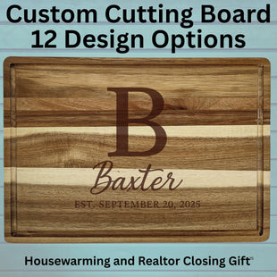 Custom engraved acacia wood cutting board with a large letter “B,” the name “Baxter,” and the text “Est. September 20, 2025.” The background features light blue wooden planks. Text above the board reads “Custom Cutting Board – 12 Design Options,” and text below reads “Housewarming and Realtor Closing Gift.”