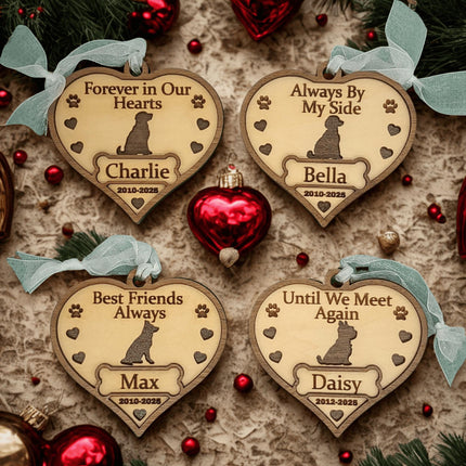 Four heart-shaped wooden dog memorial ornaments displayed on a festive surface with red ornaments and evergreen accents. Each ornament is engraved with a dog silhouette, paw prints, and hearts, featuring different sentiments: “Forever in Our Hearts” (Charlie, 2010–2025), “Always By My Side” (Bella, 2010–2025), “Best Friends Always” (Max, 2010–2025), and “Until We Meet Again” (Daisy, 2012–2025).