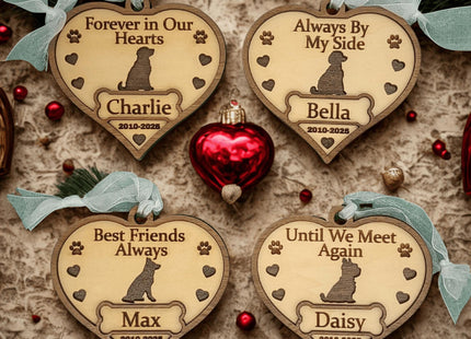Four heart-shaped wooden dog memorial ornaments displayed on a festive surface with red ornaments and evergreen accents. Each ornament is engraved with a dog silhouette, paw prints, and hearts, featuring different sentiments: “Forever in Our Hearts” (Charlie, 2010–2025), “Always By My Side” (Bella, 2010–2025), “Best Friends Always” (Max, 2010–2025), and “Until We Meet Again” (Daisy, 2012–2025).