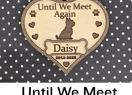 Heart-shaped wooden dog memorial ornament engraved with “Until We Meet Again,” featuring a dog silhouette, paw prints, and hearts. The ornament includes the name “Daisy” and dates “2012–2025,” with a white ribbon for hanging, displayed against a black background with white polka dots. Text below reads “Until We Meet Again.”