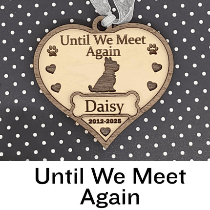 Heart-shaped wooden dog memorial ornament engraved with “Until We Meet Again,” featuring a dog silhouette, paw prints, and hearts. The ornament includes the name “Daisy” and dates “2012–2025,” with a white ribbon for hanging, displayed against a black background with white polka dots. Text below reads “Until We Meet Again.”