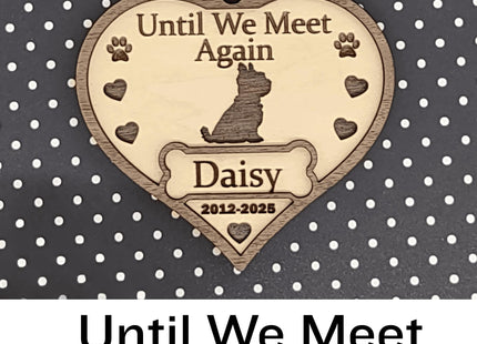 Heart-shaped wooden dog memorial ornament engraved with “Until We Meet Again,” featuring a dog silhouette, paw prints, and hearts. The ornament includes the name “Daisy” and dates “2012–2025,” with a white ribbon for hanging, displayed against a black background with white polka dots. Text below reads “Until We Meet Again.”