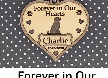 Heart-shaped wooden dog memorial ornament engraved with “Forever in Our Hearts,” featuring a dog silhouette, paw prints, and hearts. The ornament includes the name “Charlie” and dates “2010–2025,” with a white ribbon for hanging, displayed against a black background with white polka dots. Text below reads “Forever in Our Hearts.”