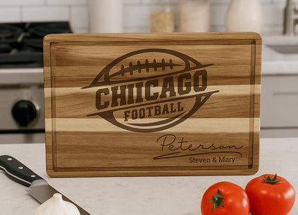 “Personalized Chicago football cutting board made from striped acacia wood, engraved with a football logo and the family name ‘Peterson – Steven & Mary.’ Displayed upright on a kitchen counter with garlic, tomatoes, a knife, and cooking utensils in the background, emphasizing its decorative and functional appeal.”