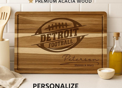 “Personalized Detroit football cutting board made from premium acacia wood, engraved with a football logo and the name ‘Peterson – Steven & Mary.’ Displayed on a kitchen counter with olive oil, utensils, and a cloth. Text above reads ‘Custom Cutting Board – Premium Acacia Wood’ and below, ‘Personalize with Your Name.’”
