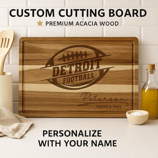 “Personalized Detroit football cutting board made from premium acacia wood, engraved with a football logo and the name ‘Peterson – Steven & Mary.’ Displayed on a kitchen counter with olive oil, utensils, and a cloth. Text above reads ‘Custom Cutting Board – Premium Acacia Wood’ and below, ‘Personalize with Your Name.’”